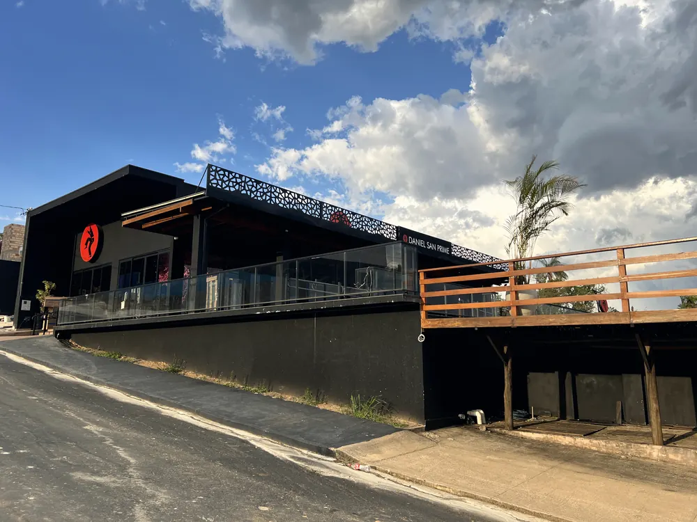 Fachada do restaurante Daniel San Prime, com varanda de vidro e deck de madeira